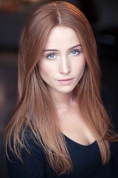 a woman with long red hair and blue eyes posing for a headshot in front of a black background