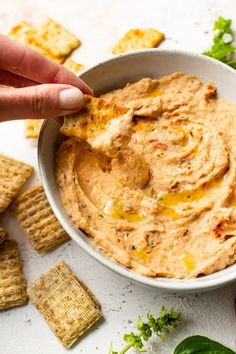 a hand dipping a cracker into a bowl of hummus and tortilla chips