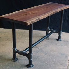 a wooden table sitting on top of a cement floor next to pipe pipes and a black wall