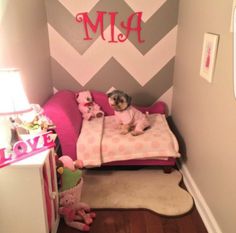 a small child's room with pink and gray walls, chevroned wallpaper and a dog on the bed