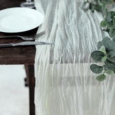 the table is set with white plates and silverware, greenery, and napkins