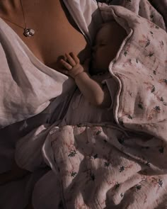 a baby wrapped in a blanket laying on top of a woman's chest and wearing a necklace