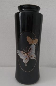 a black vase with a butterfly painted on the side and gold trim around the bottom