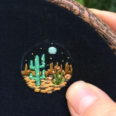 someone is stitching a cactus patch on a black cloth