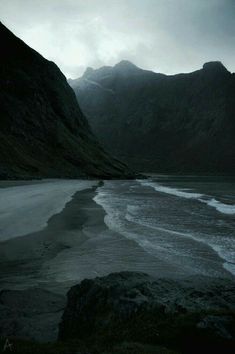 an empty beach with mountains in the background and water on the sand at the bottom