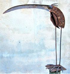 a metal bird with long legs standing on top of a wooden table next to a wall