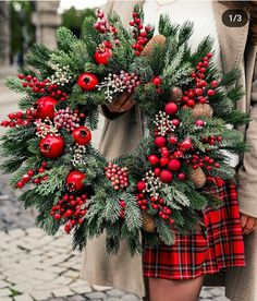 a woman holding a christmas wreath with red berries and pine cones