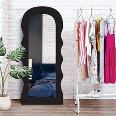 a mirror sitting on top of a wooden floor next to a white shelf filled with clothes