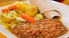 a white plate topped with meat and veggies next to a rolled up burrito