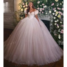 a woman in a ball gown standing next to a flower covered wall with flowers on it