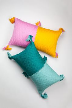 three colorful pillows with tassels on them sitting next to each other in front of a white background