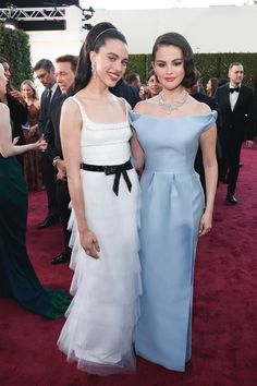 two women standing next to each other on a red carpet with people in the background