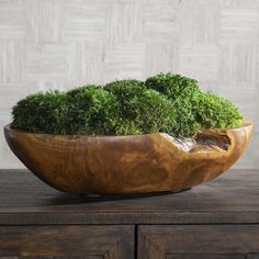 a wooden bowl filled with green plants on top of a table