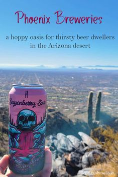 a person holding up a can of beer in front of a desert landscape with cacti