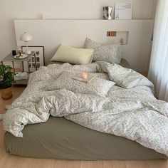 an unmade bed in a bedroom with white walls and wooden floors, along with a plant