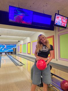 a woman holding a red bowling ball in her right hand and posing for the camera