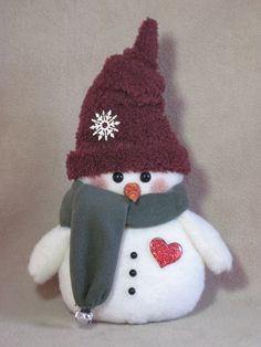 a stuffed snowman wearing a red hat and scarf with a heart on it's chest