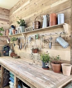 a wooden table topped with lots of pots and pans next to a shelf filled with potted plants