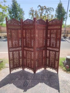 an intricately carved wooden room divider sitting on the side of a road with trees in the background