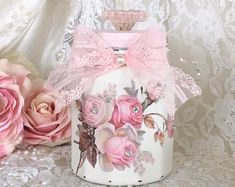 two pink roses are sitting next to a white lace covered table cloth and a jar