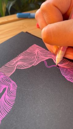 a person is drawing on a piece of black paper with pink and purple lines in it