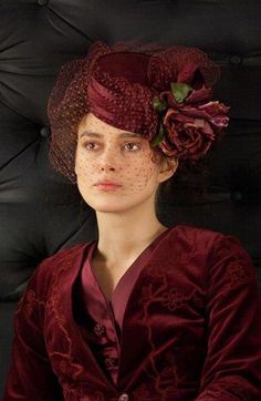 a woman wearing a red dress and hat with flowers on it's head, sitting in front of a black background