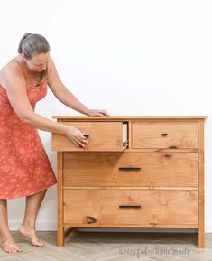 a woman in an orange dress standing next to a wooden dresser with drawers on it