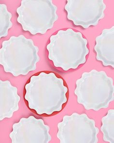 many white plates are arranged on a pink background with one red plate in the middle