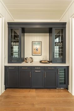 an empty kitchen with black cabinets and wood flooring in front of a painting on the wall