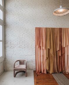 a chair sitting in front of a brick wall next to a window with curtains on it