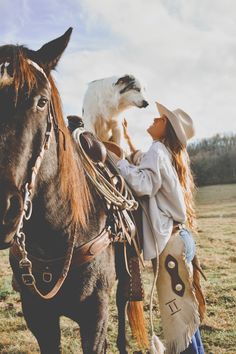 a woman is standing next to a horse with a dog on her back