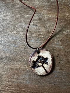 a necklace with a tree on it sitting on top of a wooden table next to a cord