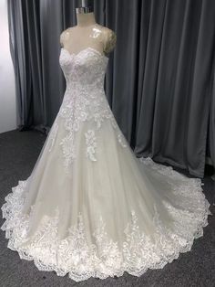 a white wedding dress on display in front of a gray curtained window with curtains behind it