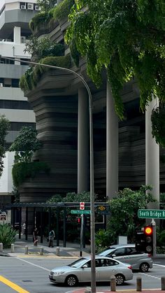 cars are driving down the street in front of tall buildings with green plants growing on them