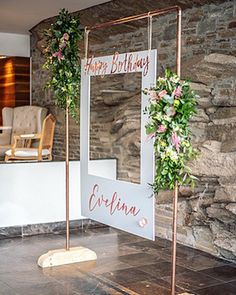 a sign that says happy birthday next to some flowers and greenery on the side of a stone wall