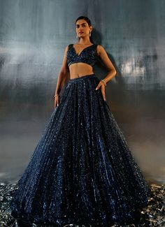 This stunning Blue Sequins Embroidered Bridal Lehenga Set is the epitome of elegance and modernity. Crafted from soft net fabric, the blue lehenga is adorned with intricate abstract motifs, dazzling with tonal sequins, crystals, and bugle beads that catch the light beautifully. The floor-length skirt flows gracefully with every step, exuding a timeless charm. Teamed with a luxurious blouse featuring a flattering plunging neckline and voluminous design, this ensemble is completed with a matching dupatta, elegantly embellished along the border. Perfect for the bride or bride-to-be for a Cocktail or Reception, this lehenga set promises to make you stand out with its exquisite craftsmanship and contemporary allure. Composition : Lehenga, Blouse and Dupatta - Net Care: Dry Clean Only and Vacuum Elegant Blue Lehenga With Sequins, Blue Sequined Lehenga For Party, Blue Evening Lehenga, Blue Embellished Lehenga For Evening, Blue Embellished Evening Lehenga, Embellished Blue Lehenga For Evening, Blue Lehenga With Zari Work For Evening, Blue Bollywood Lehenga For Party, Blue Semi-stitched Sharara For Evening