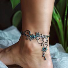 a woman's foot with a blue and green flower design on the ankle bracelet