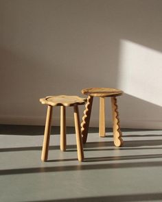 two small wooden stools sitting next to each other on a gray floor in front of a white wall