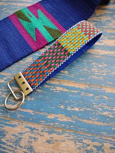 a colorful belt with a metal buckle on it sitting on a wooden table next to a pair of scissors