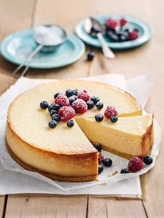 a cheesecake with blueberries and raspberries on top sits on a table