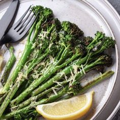 a white plate topped with asparagus and lemon wedges next to a fork