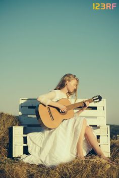 a woman sitting on top of a white bench holding a guitar in her hand and looking at the sky