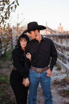 a man and woman standing next to each other in front of a wooden fence wearing cowboy hats