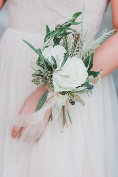 a woman wearing a white dress holding a bouquet of flowers and greenery in her hand