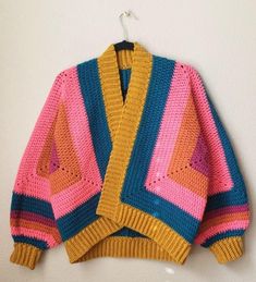 a colorful knitted sweater hanging on a white wall next to a coat hanger