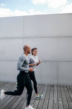 two people running on a wooden floor in front of a white wall and blue sky