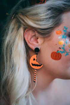 a woman with painted face and ear piercings wearing halloween decorations on her face, looking to the side