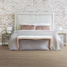 a white bed sitting in front of a brick wall next to a night stand with two nightstands