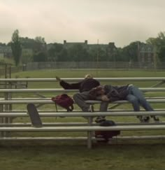 two people laying on benches in a field