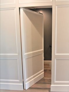 an open door in the middle of a room with white walls and wood flooring